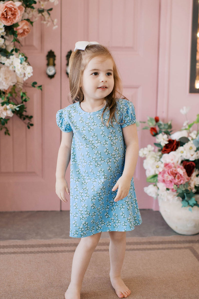 Girl wearing blue hydrangea print play apron dress with puff sleeves.