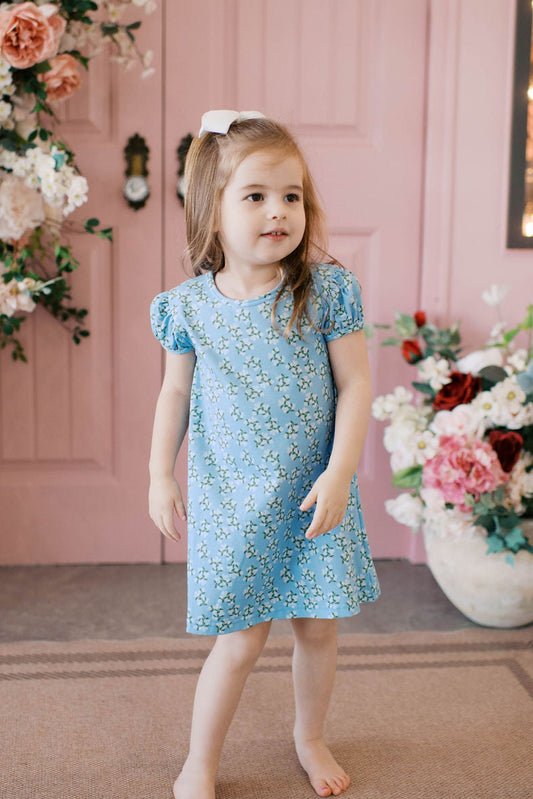 Girl wearing blue hydrangea print play apron dress with puff sleeves.